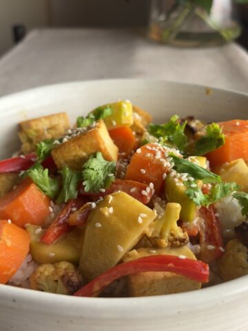 Close-up of yellow curry with tofu cubes, sweet potato, cauliflower, and carrots on rice.