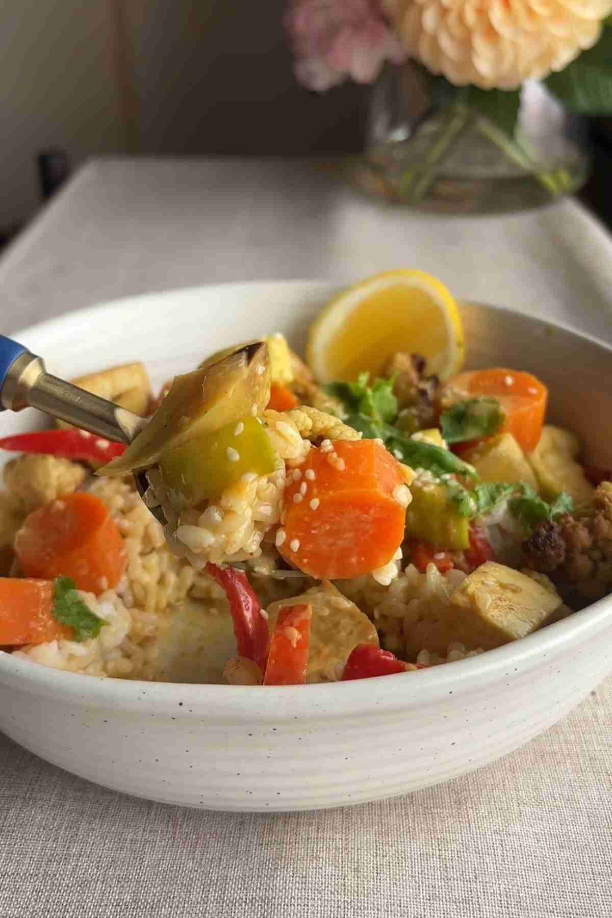 Spoon lifting yellow curry with tofu, sweet potato, cauliflower, and carrots over rice.