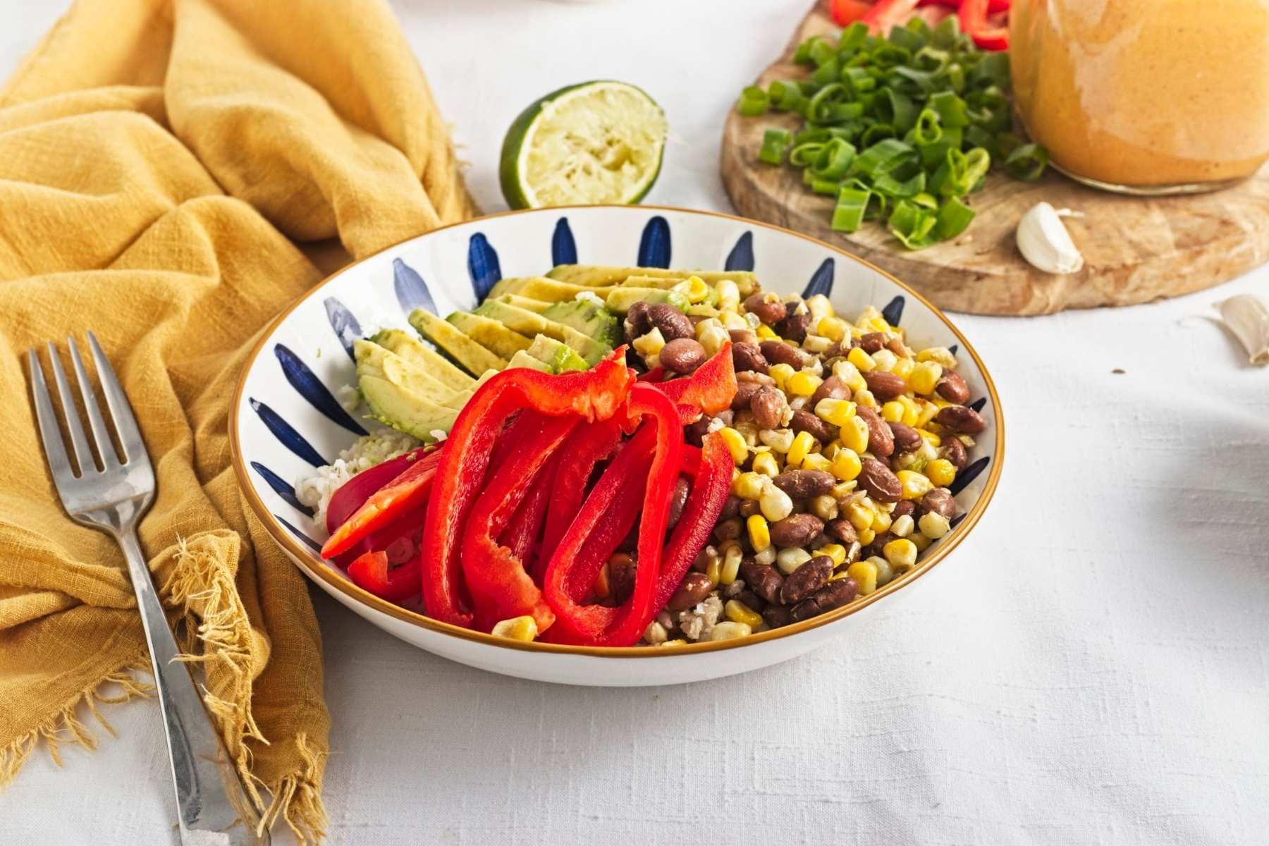 Brown rice bowl topped with corn, pinto beans, avocado, red pepper, green onions, and chipotle sauce