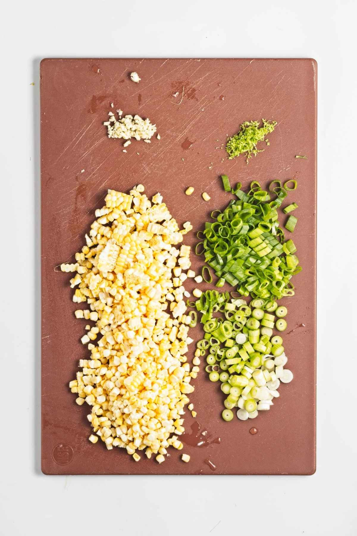 Chopped corn, sliced green onions, minced garlic, and lime zest on cutting board