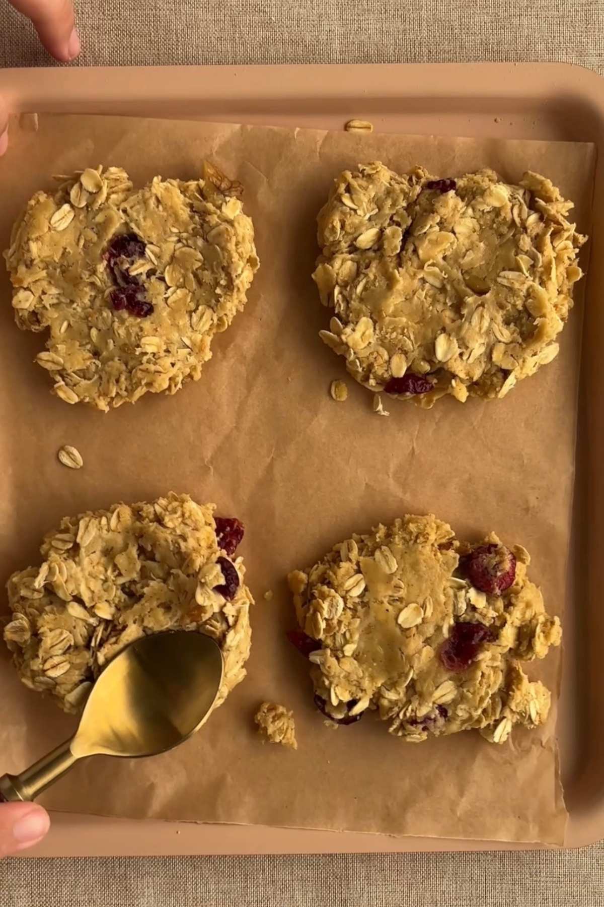 Spoon flattening oat cookie dough on a lined baking tray.