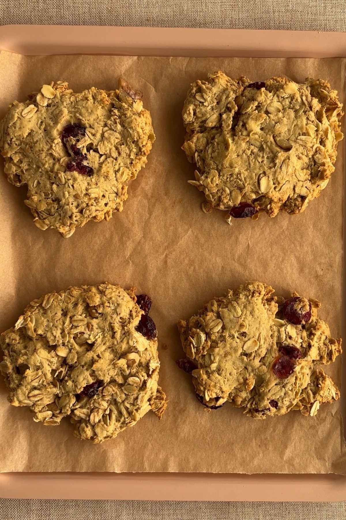 Four oat cranberry cookies on a parchment lined baking tray.
