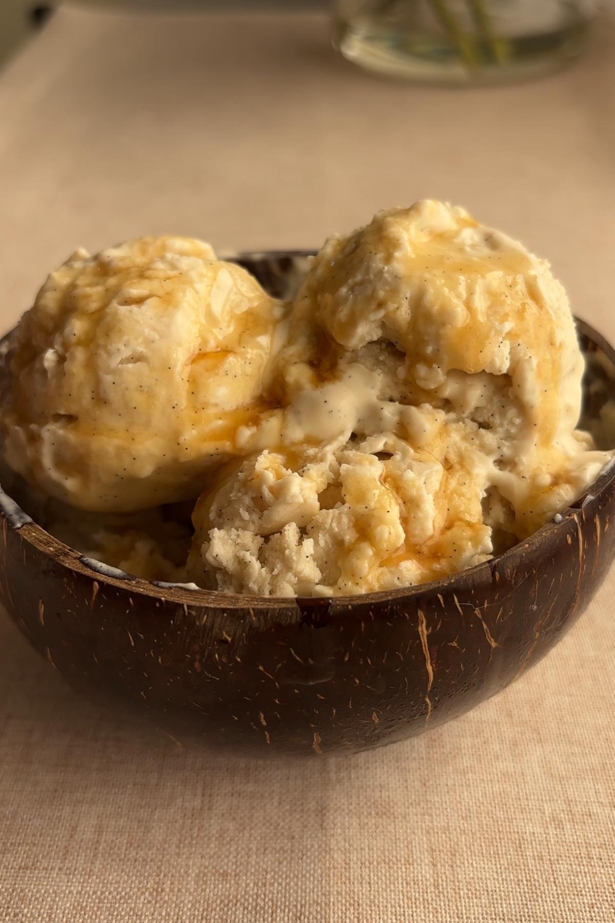 Creamy vegan coconut ice cream scooped with wooden spoon in coconut shell bowl