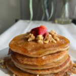 Pancake stack drizzled with syrup, strawberries, and chopped nuts.