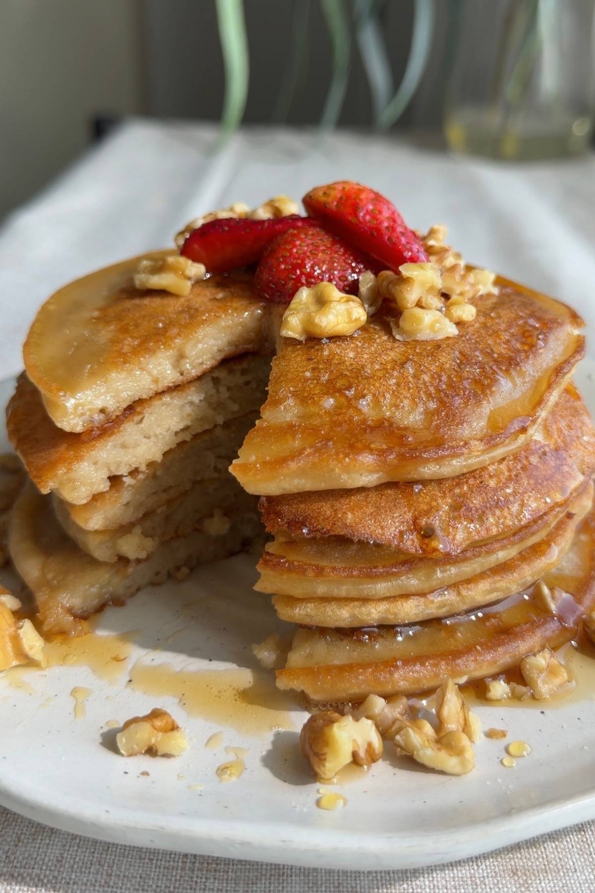 Pancake stack with a slice cut out, topped with strawberries and chopped nuts.