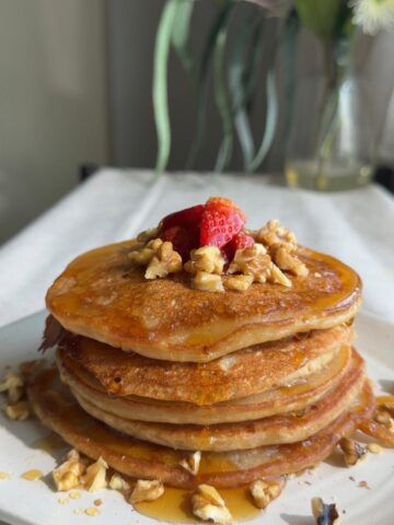Pancake stack drizzled with syrup, strawberries, and chopped nuts.