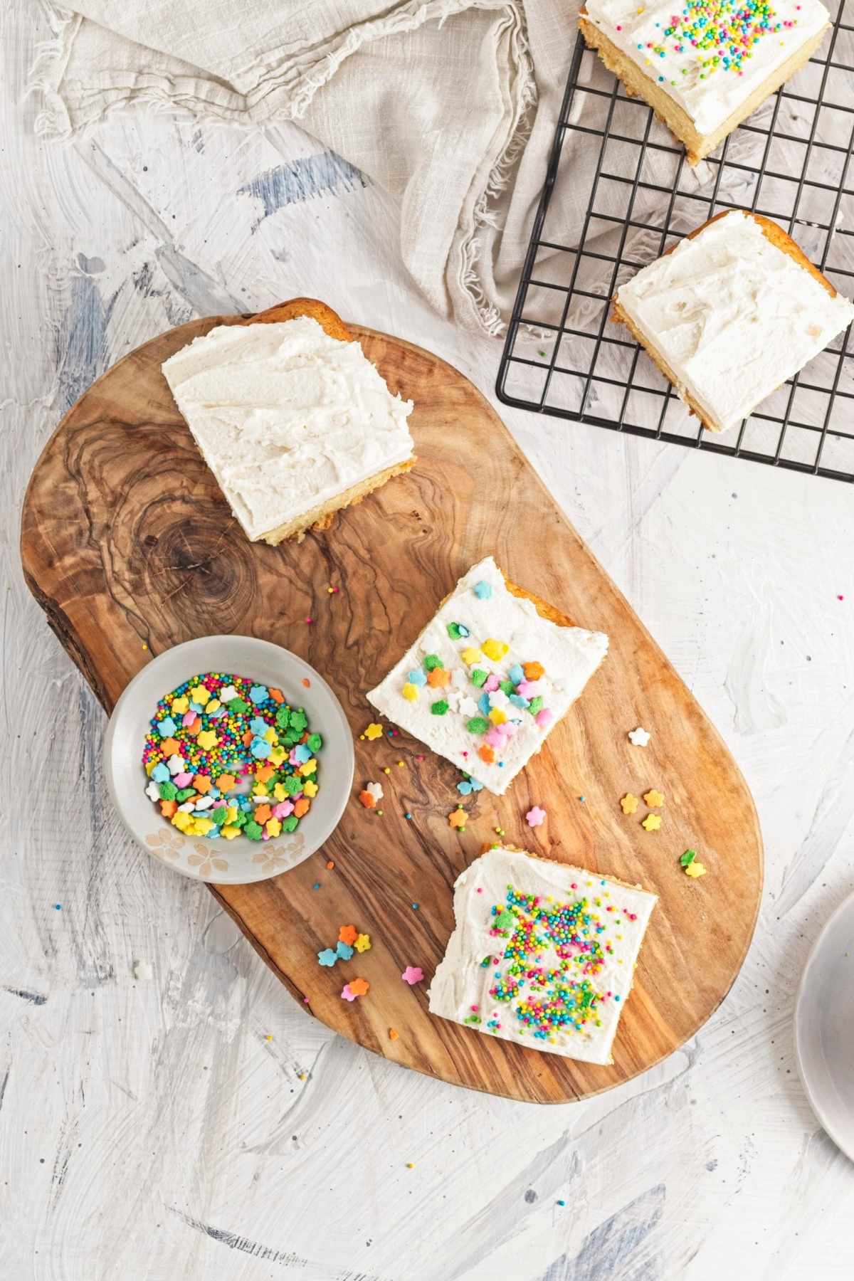 Frosted cake squares with sprinkles on a wooden board.