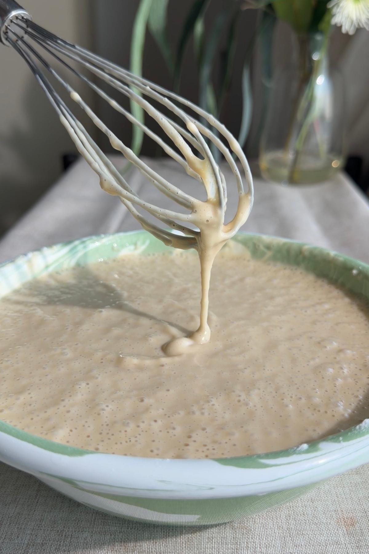 Thick batter dripping from a whisk into a mixing bowl.