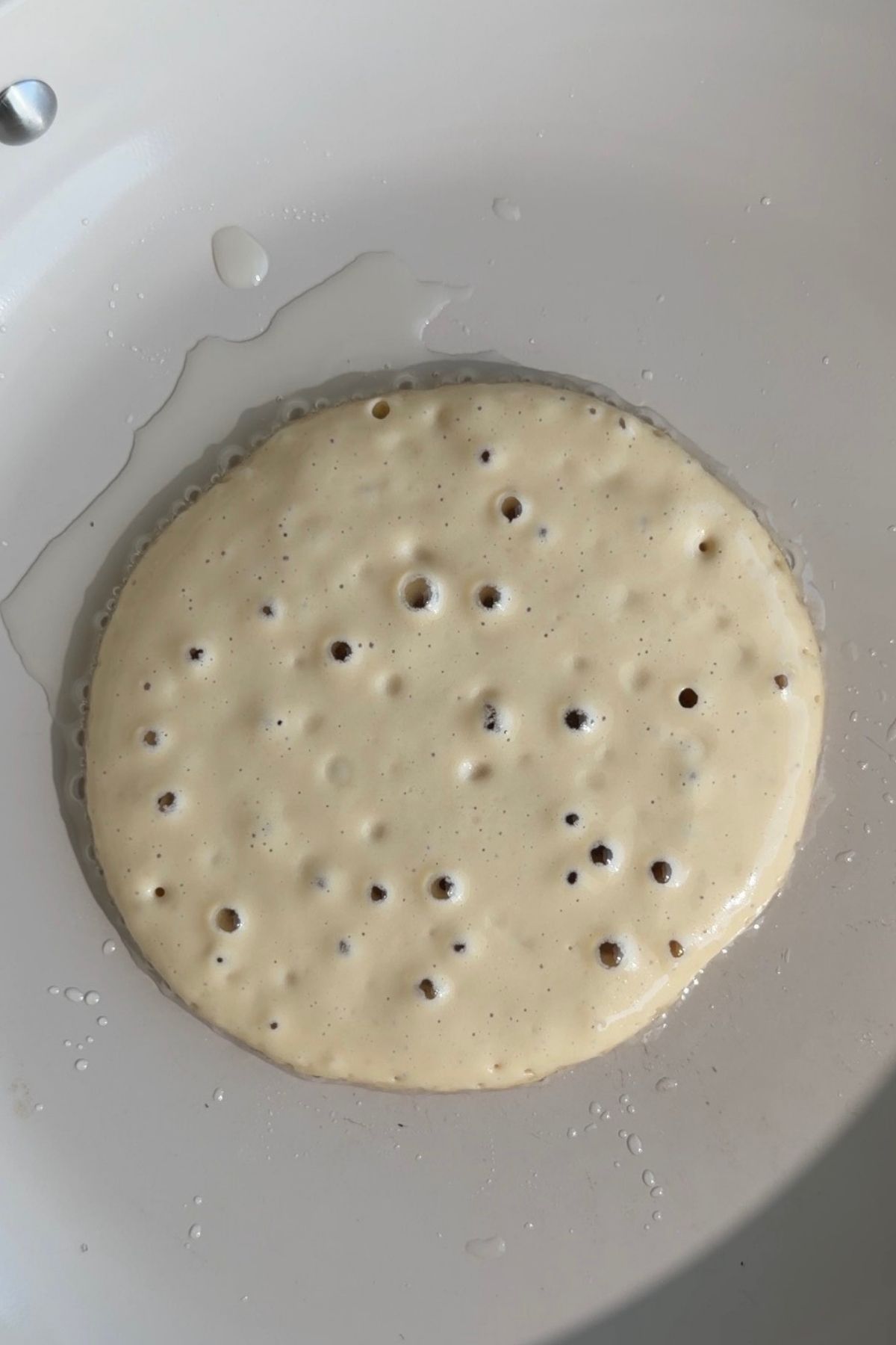 Pancake batter cooking in a pan with bubbles on the surface.