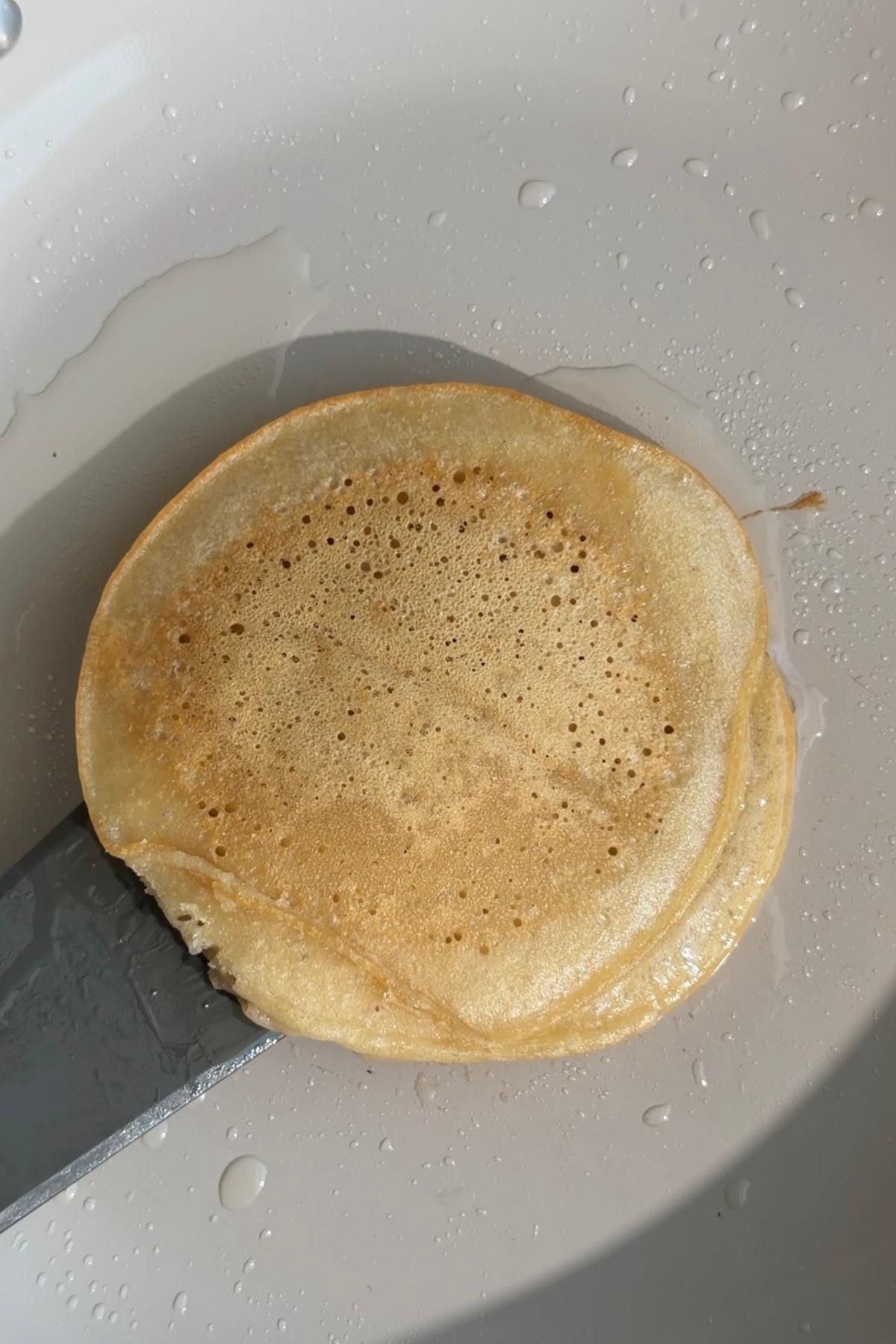 Golden pancake being lifted with a spatula in a pan.