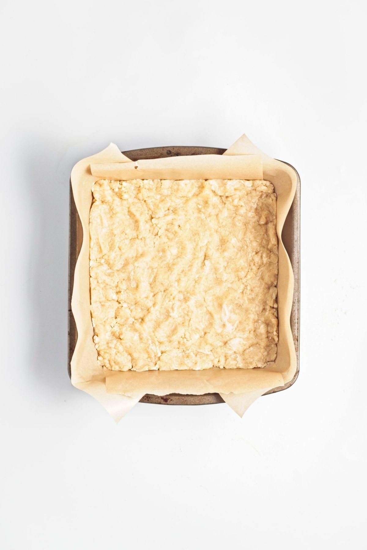 Pressed pastry base in a parchment-lined baking pan.