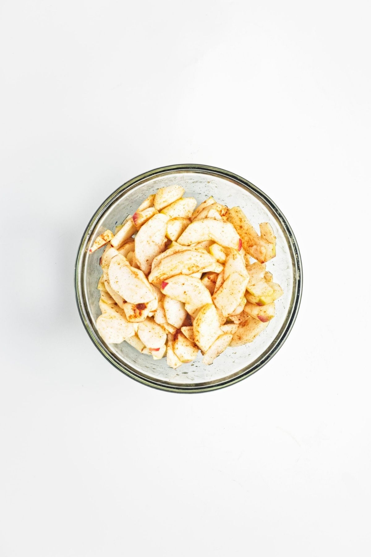 Sliced apples tossed with cinnamon in a glass bowl.