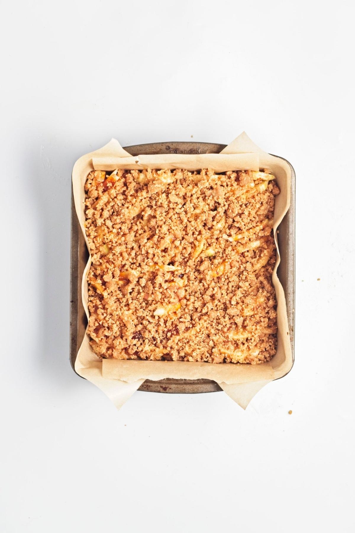 Apple crumble bars before baking in a parchment-lined pan.