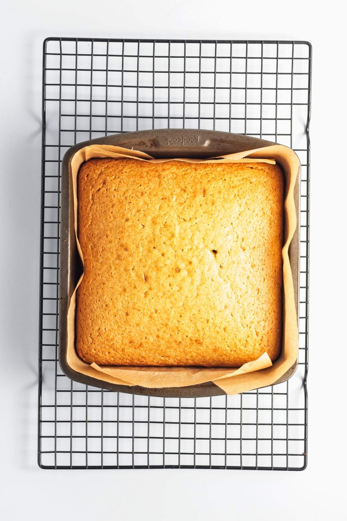 Baked square cake cooling in a parchment-lined pan.