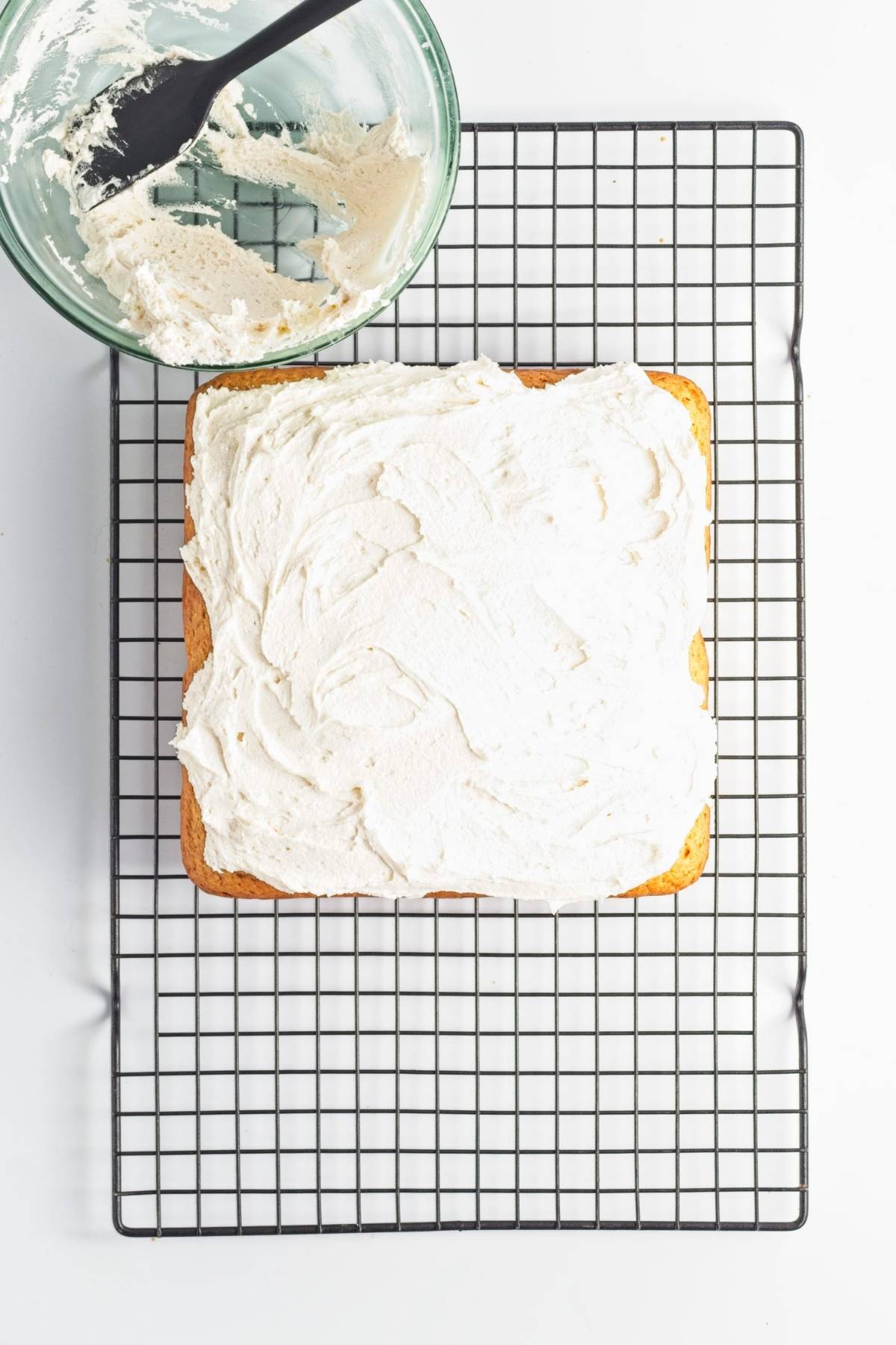 Frosting spread over a square cake on a cooling rack.