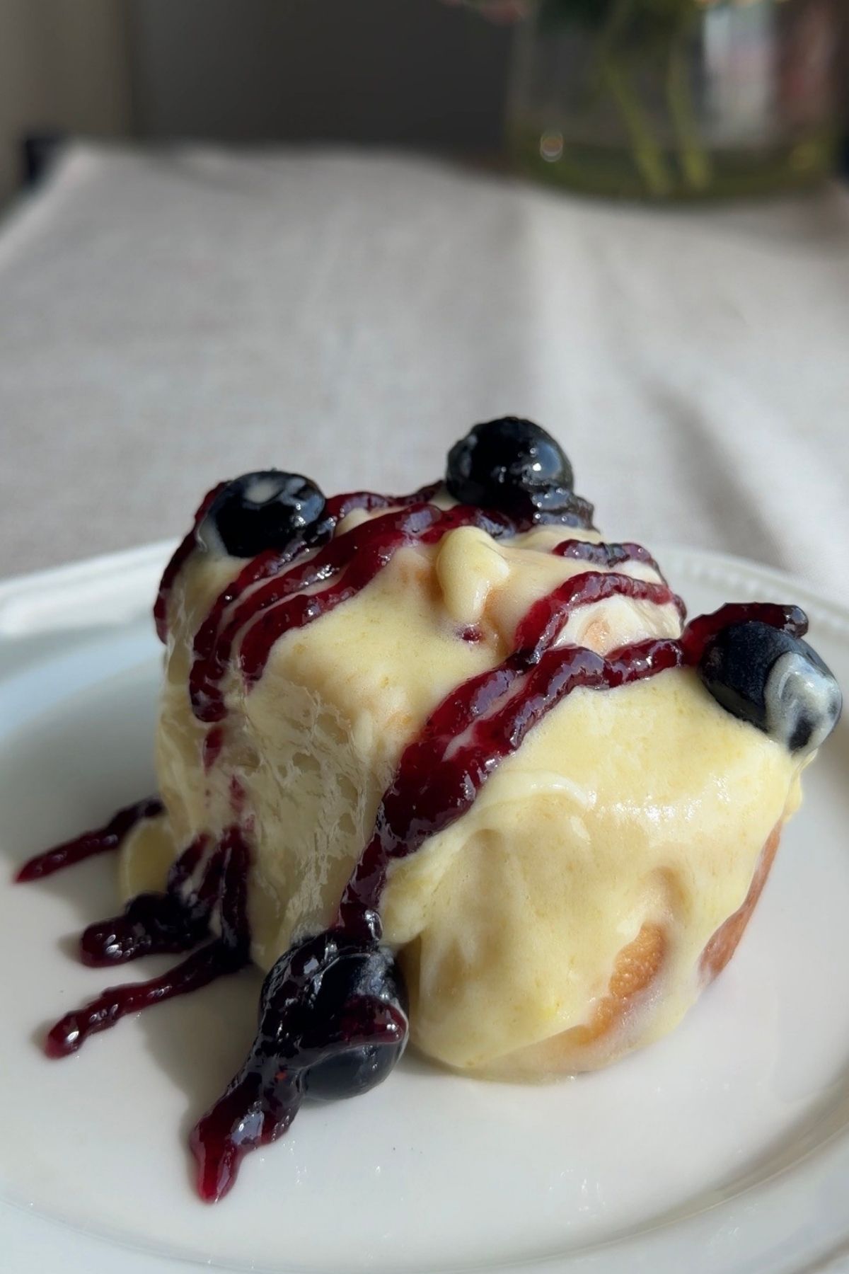 Frosted sweet roll with blueberry jam and fresh blueberries on a white plate.