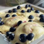 Frosted rolls topped with fresh blueberries in a white baking dish.