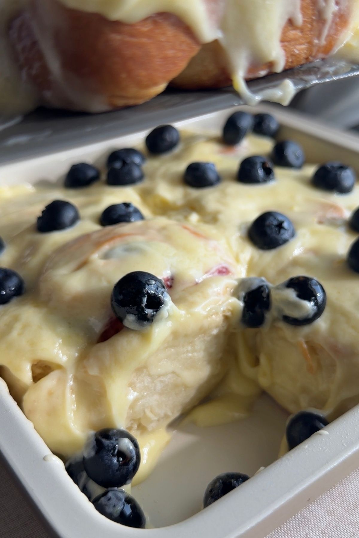 Frosted rolls topped with fresh blueberries in a white baking dish.