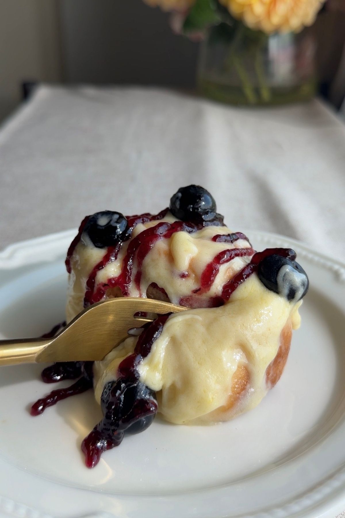 Frosted sweet roll with blueberry jam and fresh blueberries on a white plate.