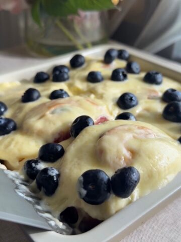Frosted rolls topped with fresh blueberries in a white baking dish.