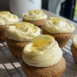 Cupcakes with lemon frosting and lemon slice garnish cooling on a wire rack.