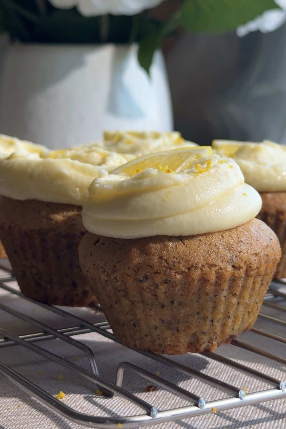 Cupcakes with lemon frosting and lemon slice garnish on a cooling rack.