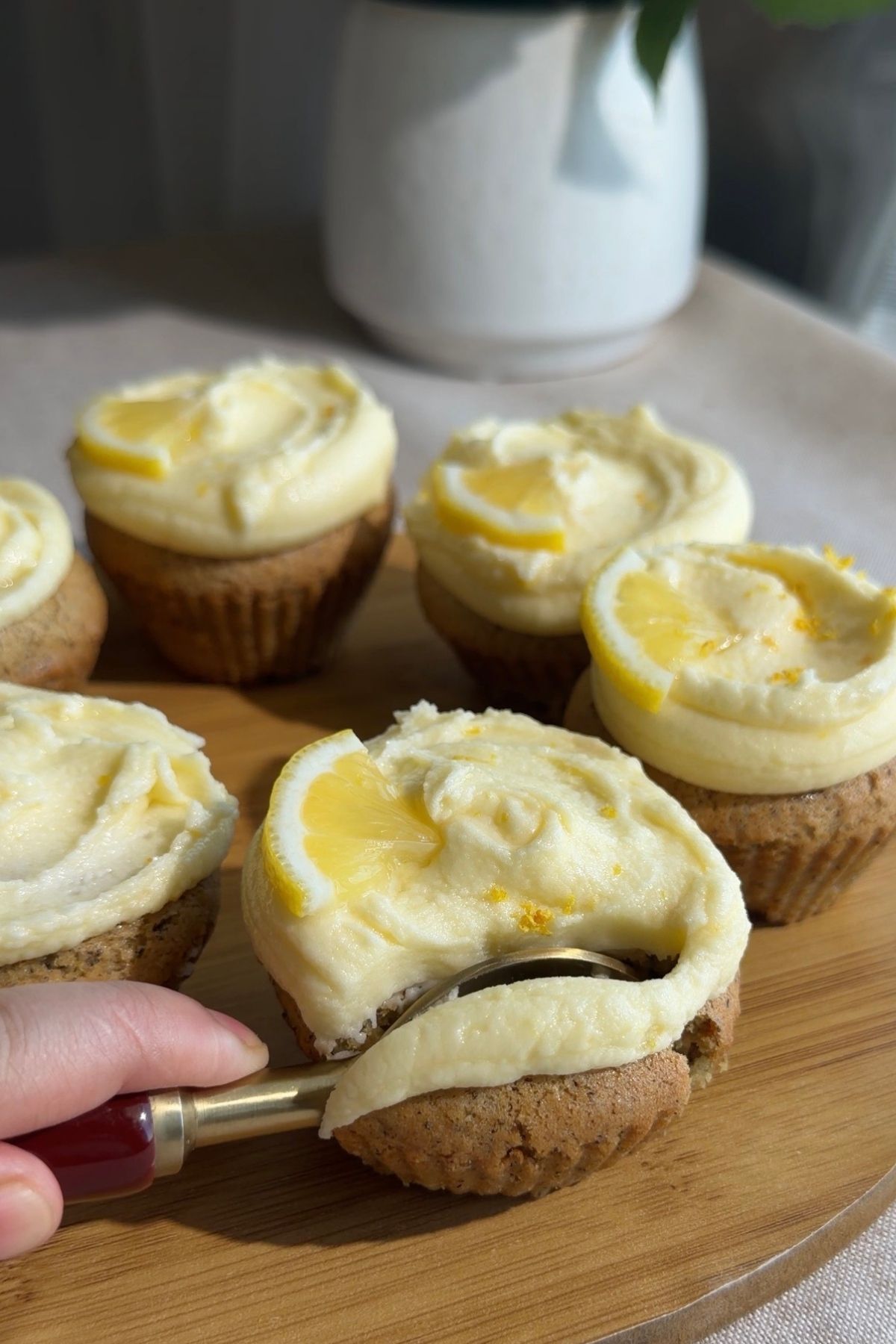 Cupcake with lemon frosting being spread using a small spoon.