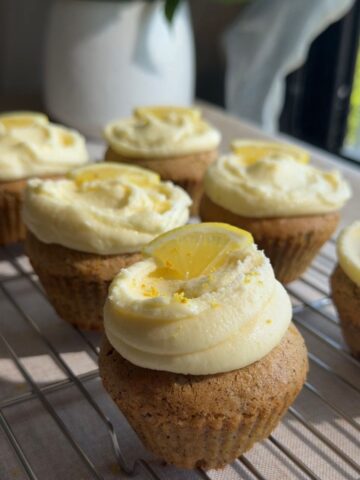 Cupcakes with lemon frosting and lemon slice garnish cooling on a wire rack.