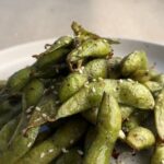 Air fried edamame pods with chili flakes served in a white bowl.