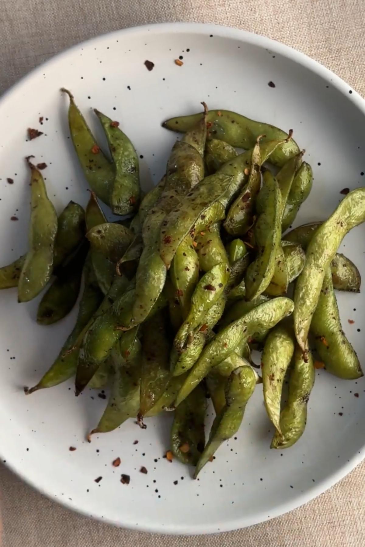 Close-up of air fried edamame pods with sesame seeds and chili flakes.