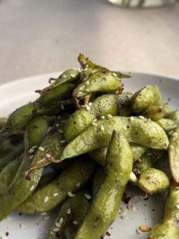 Air fried edamame pods with chili flakes served in a white bowl.