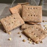 Stacked homemade crackers beside a tipped glass jar.
