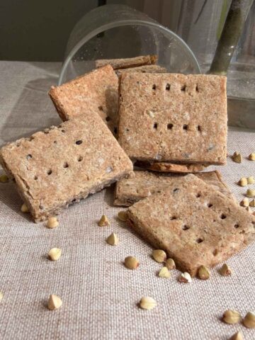 Stacked homemade crackers beside a tipped glass jar.