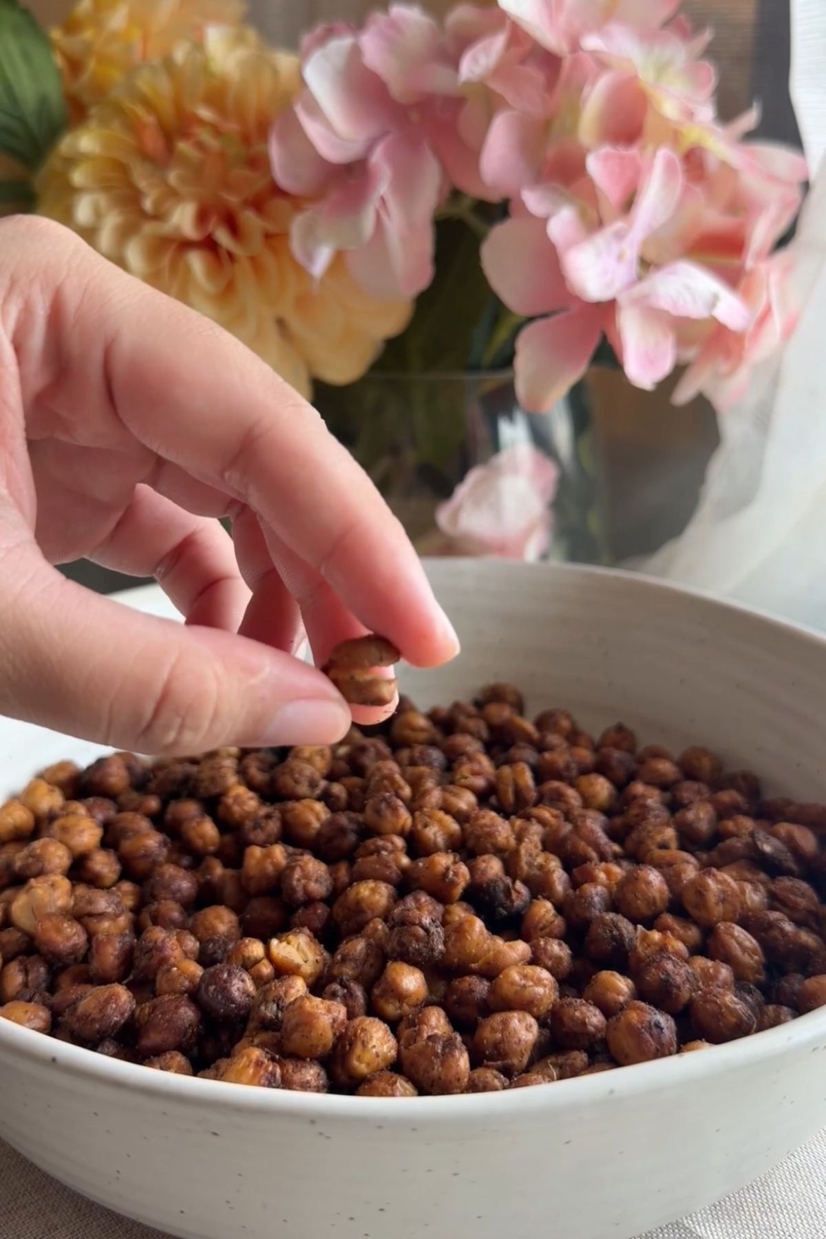 Roasted chickpeas in a white bowl with a hand reaching toward them.