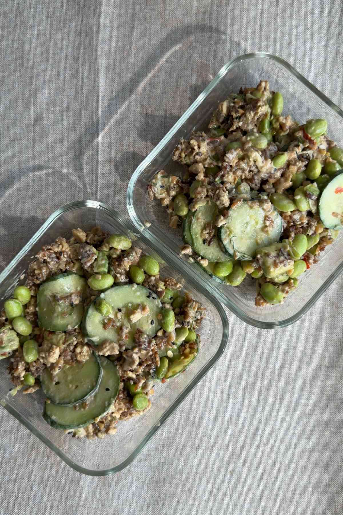 Salad portions with cucumber, edamame, crispy rice, and tofu in glass meal prep containers.