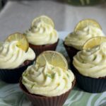 Five frosted ginger lime cupcakes garnished with lemon slices on a patterned serving plate.