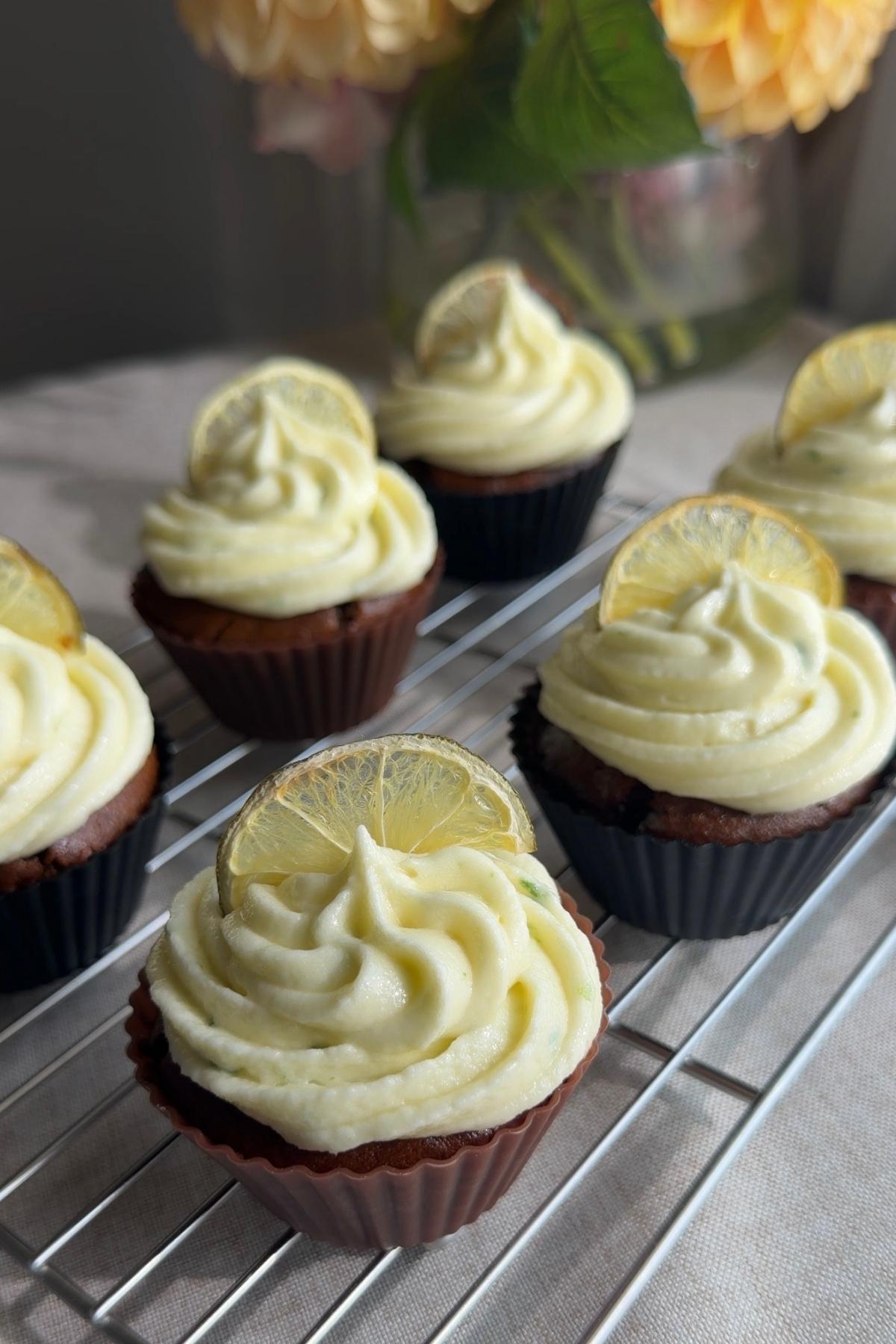 Frosted ginger lime cupcakes with citrus slice garnish arranged on a cooling rack.