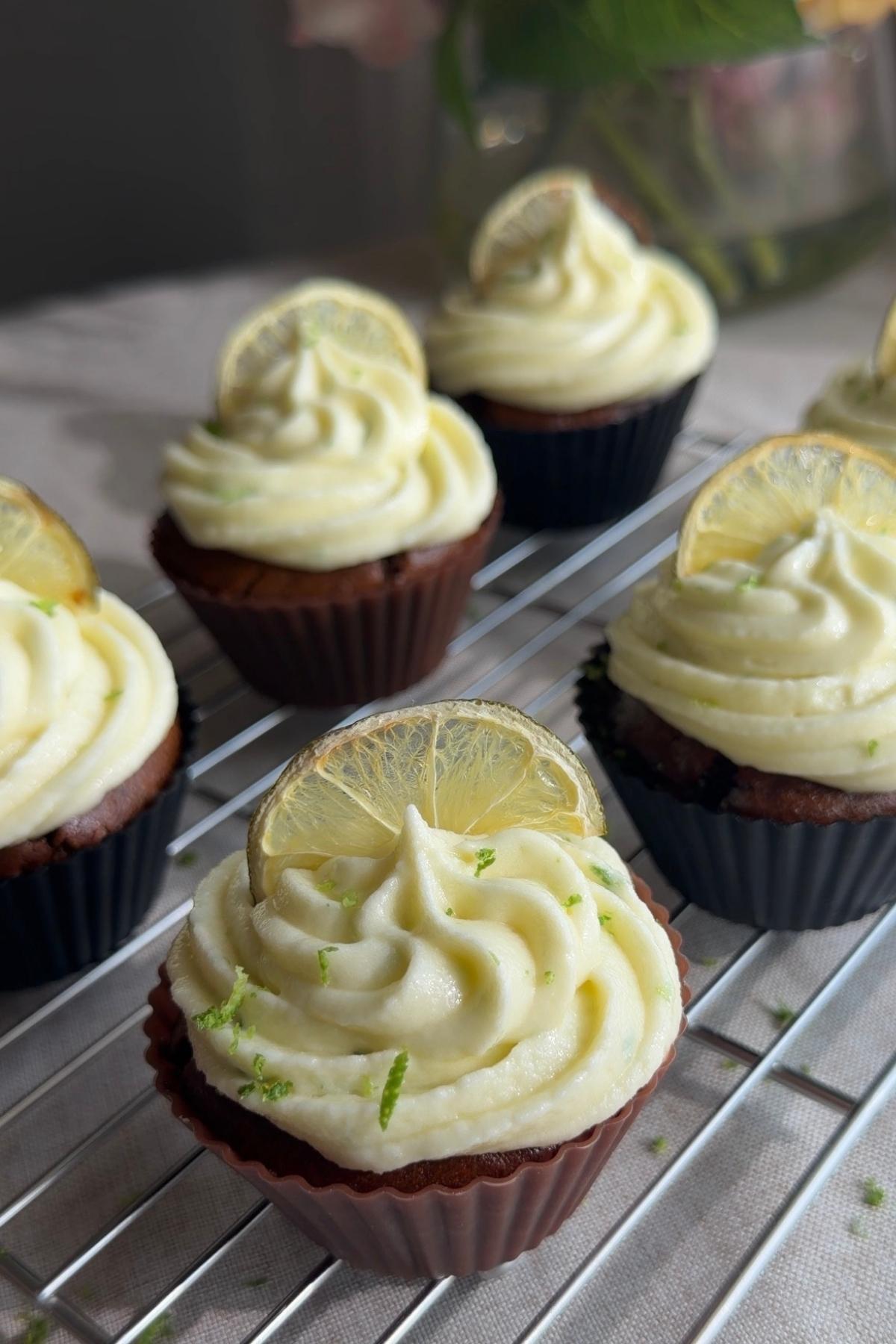 Ginger lime cupcakes topped with swirls of frosting and lemon slices on a cooling rack.