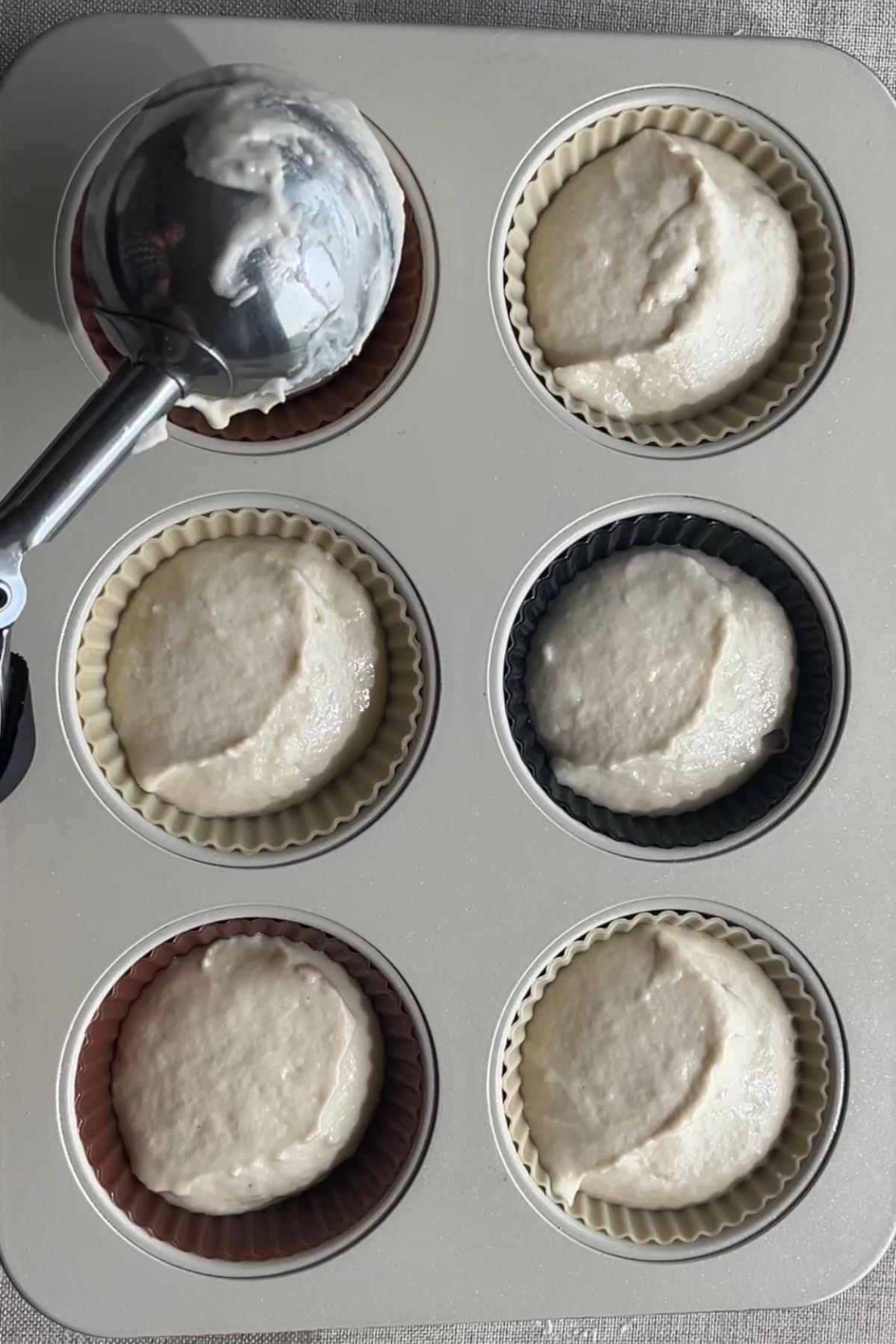 Cupcake batter being scooped into lined muffin cups.
