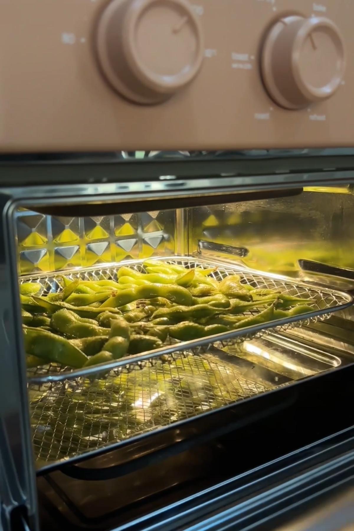 Edamame pods cooking in an air fryer basket.