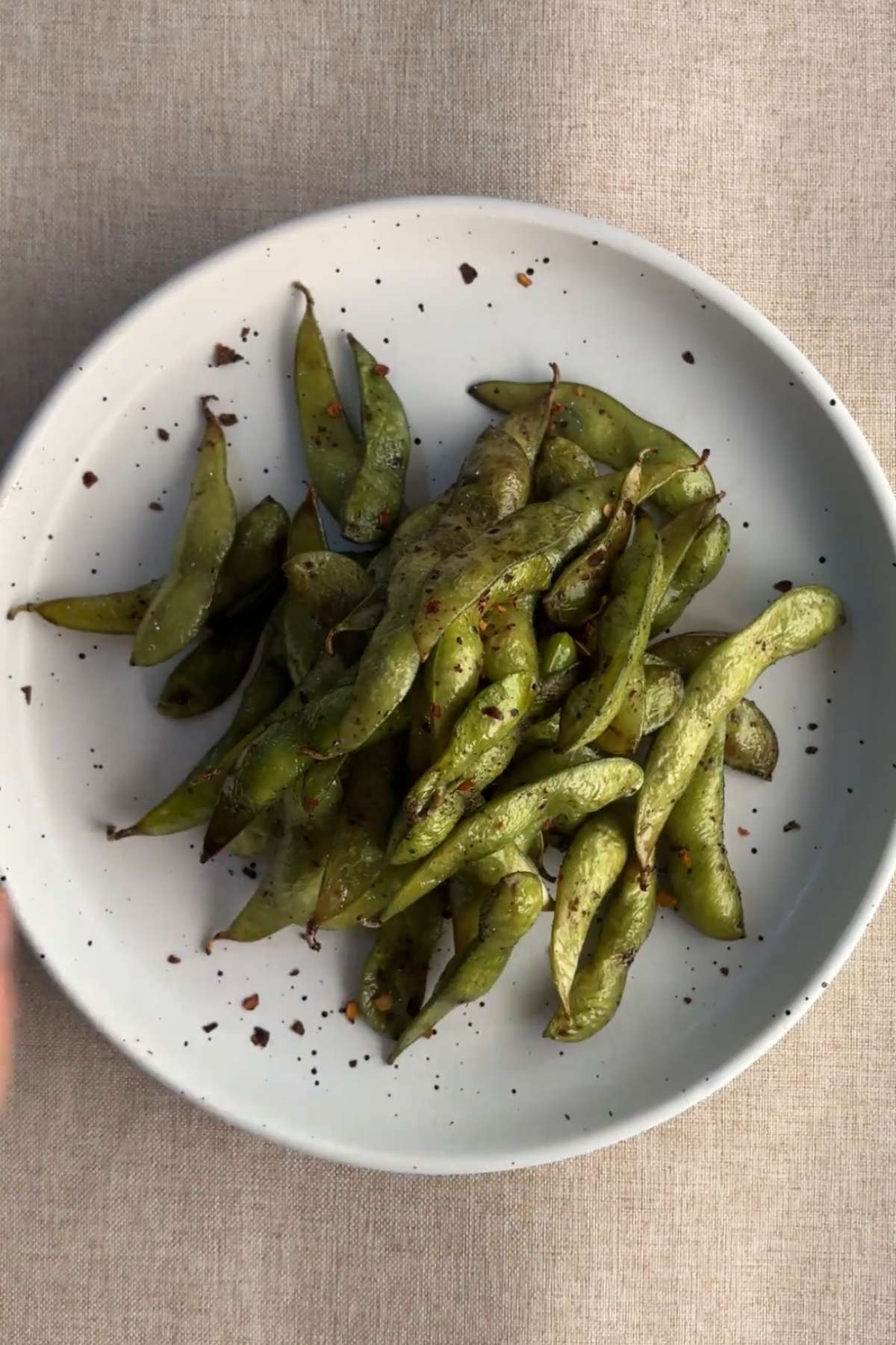 Air fried edamame pods with sesame seeds and chili flakes served in a bowl.