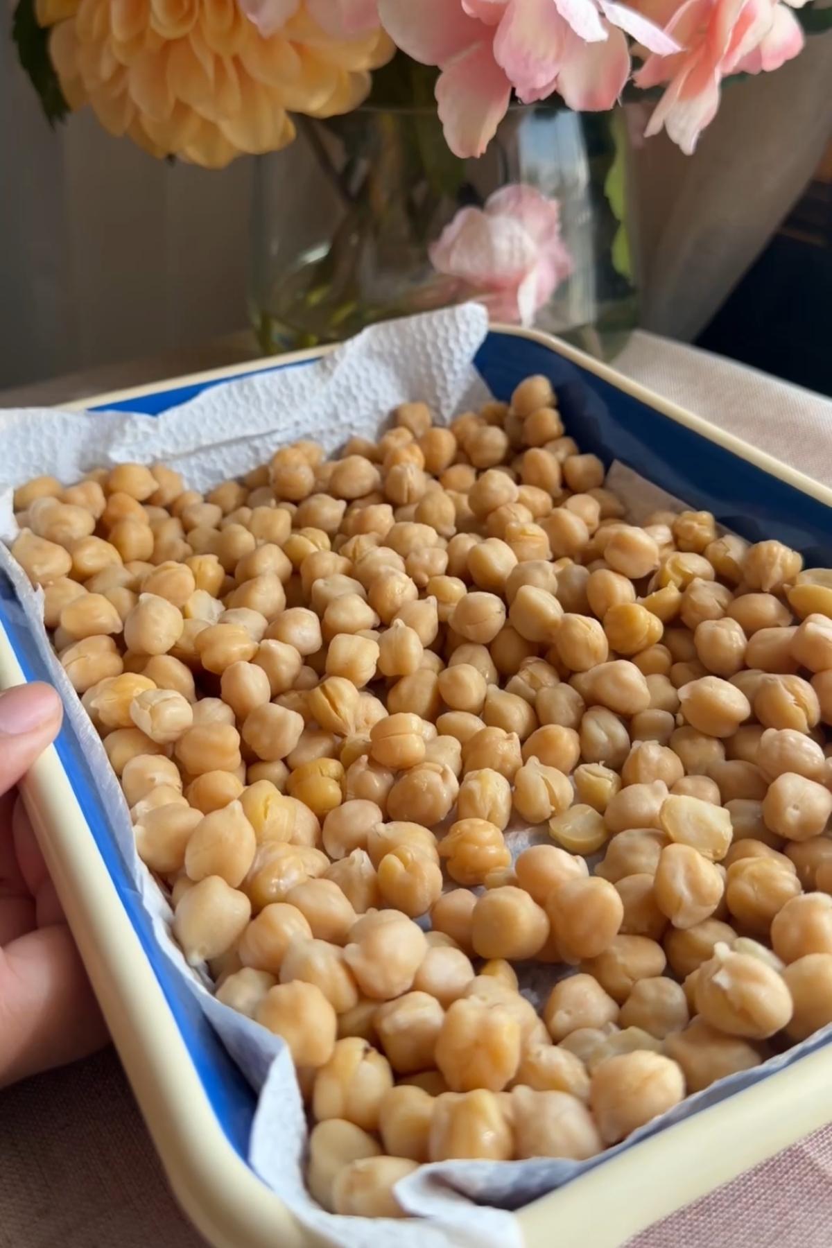 Chickpeas spread in a lined baking dish after being drained and dried.