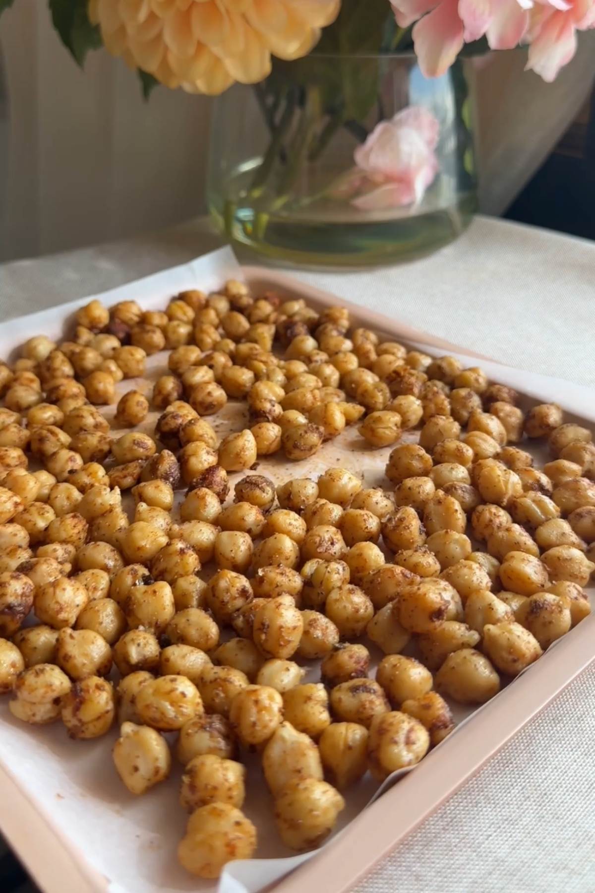 Seasoned chickpeas spread in a single layer on a parchment-lined tray.