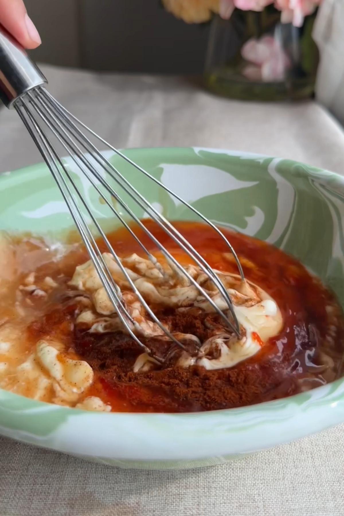 Whisking creamy dressing with chili sauce and spices in a shallow bowl.