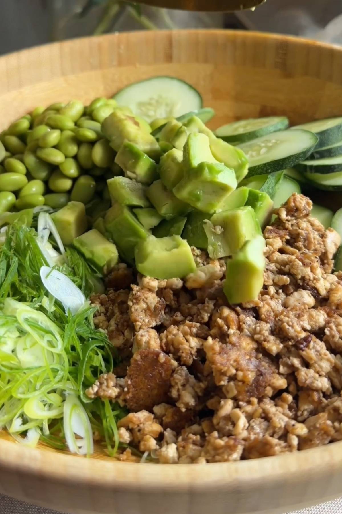 Cucumber, avocado, edamame, green onion, and crispy tofu in a serving bowl.