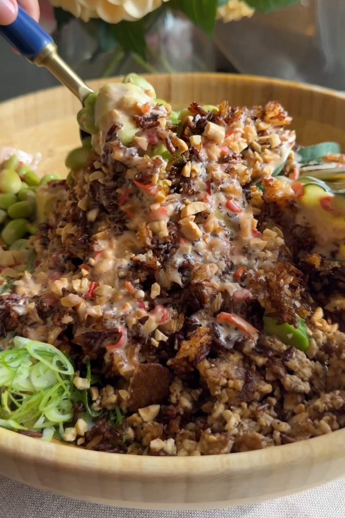 Creamy dressing being poured over crispy rice, tofu, cucumber, and edamame.
