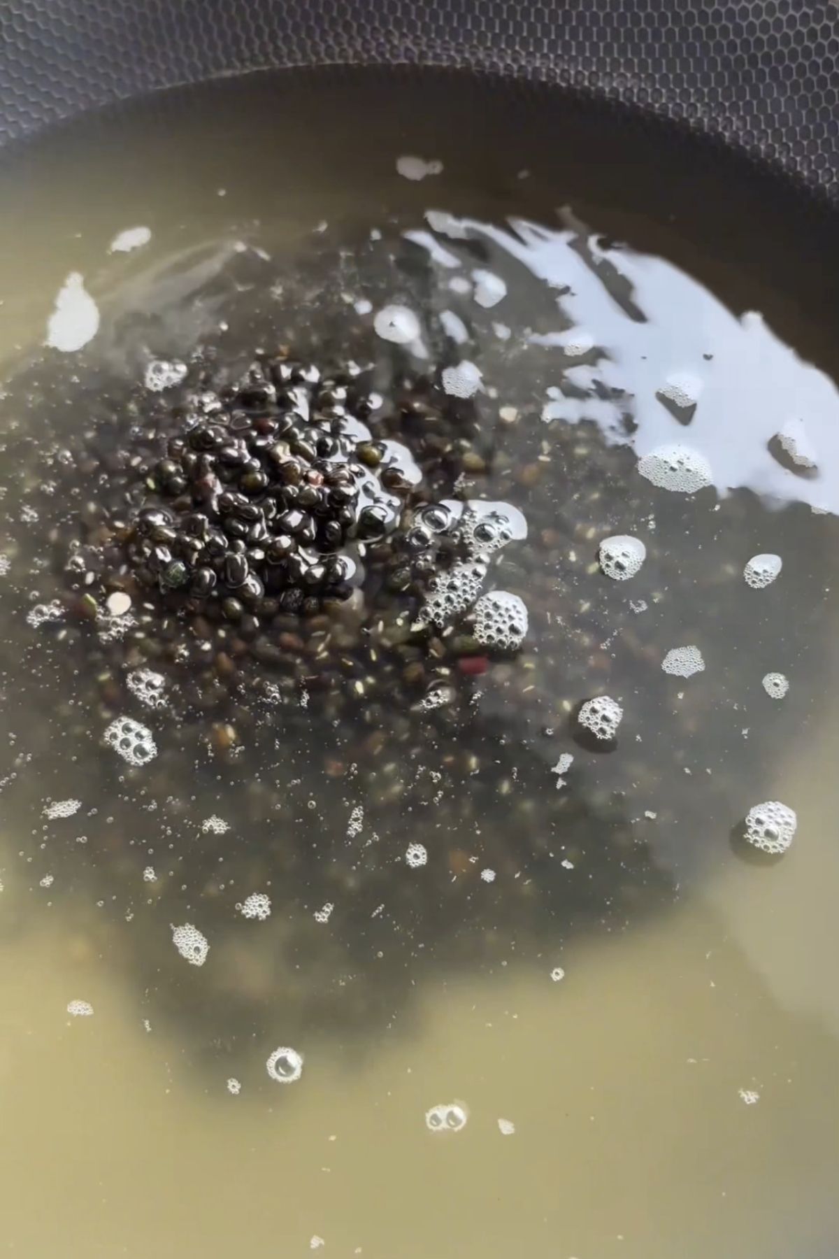 Black lentils simmering in water in a saucepan.