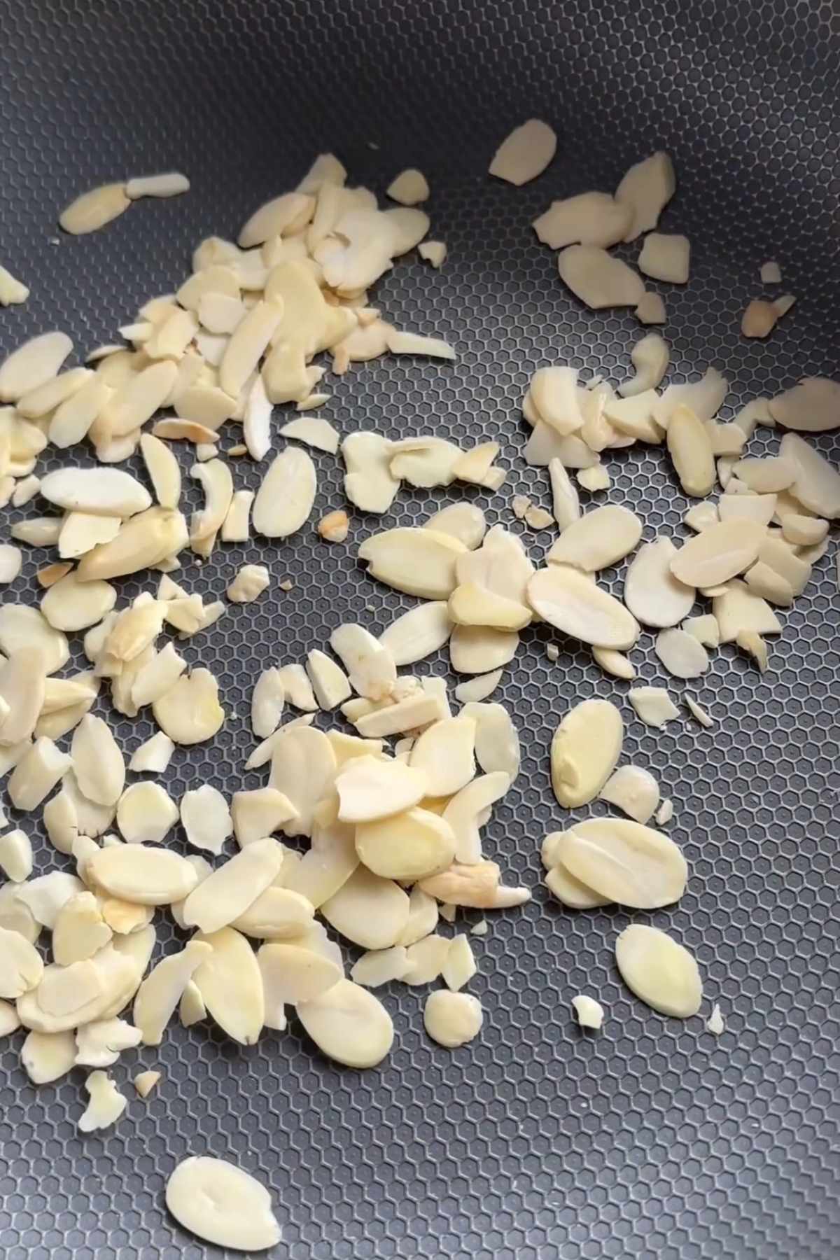 Sliced almonds toasting in a frying pan.