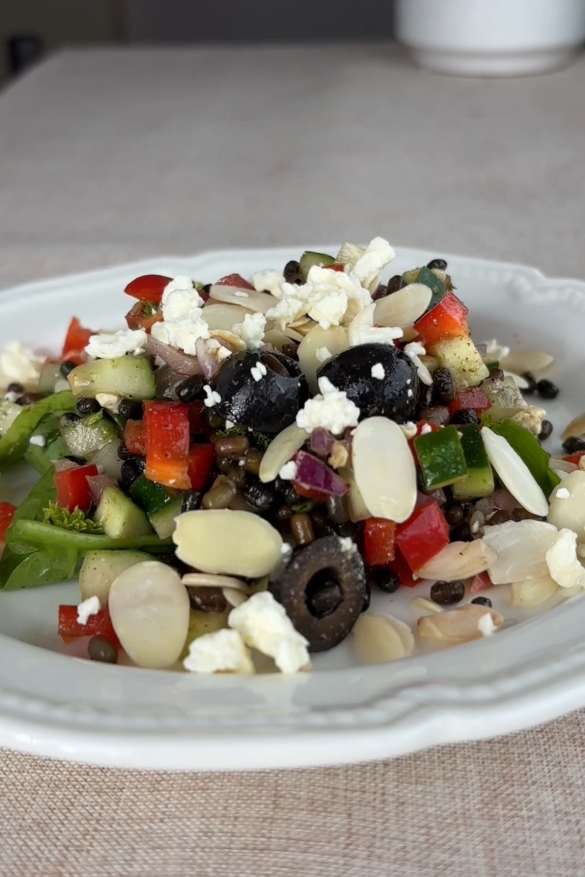 Black lentil salad tossed with greens, olives, cucumber, and red pepper in a serving bowl.