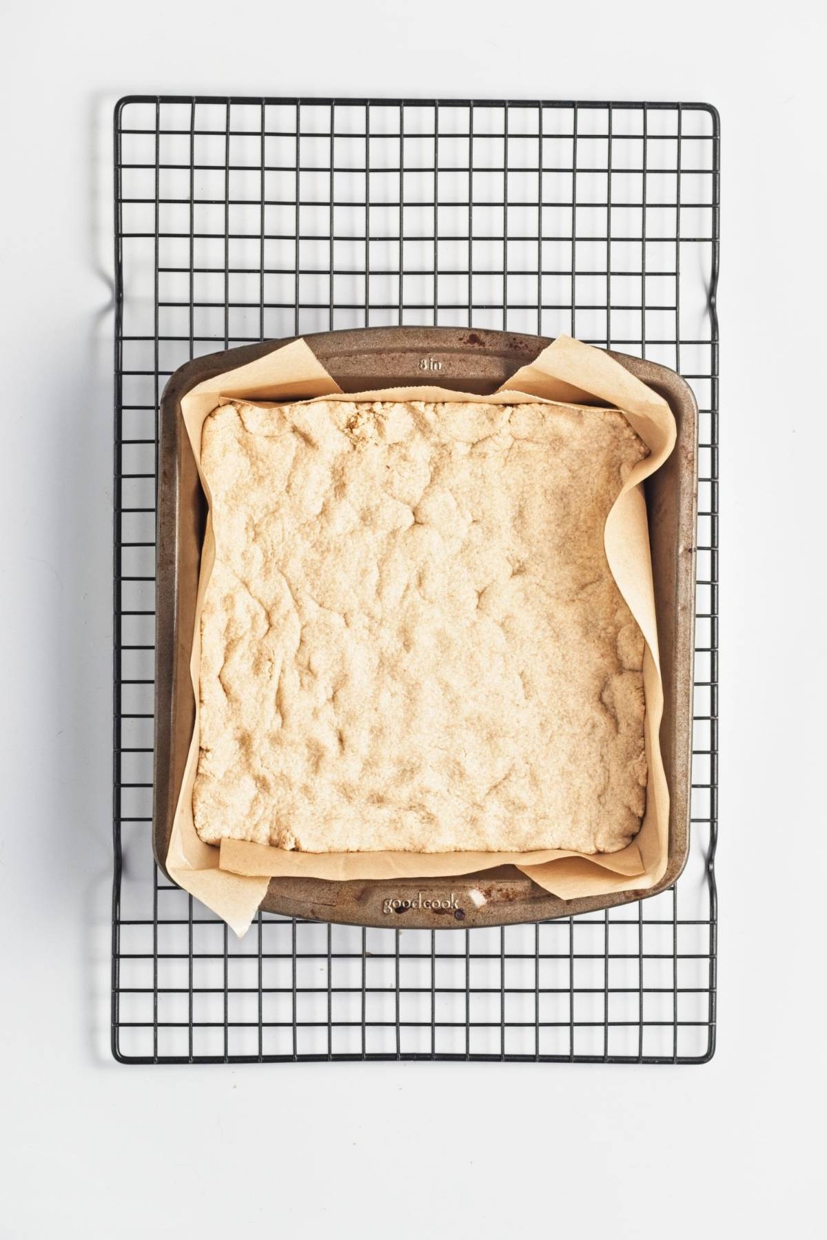 Blind-baked crust in a parchment-lined square pan on a cooling rack.